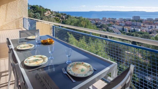 Un balcón con una mesa lista para comer, con vistas a una ciudad costera.