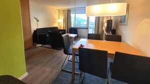 A hotel room with a dining area, a sofa, a TV, and a window with curtains. - Allod Park Haus C 604 by Interhome (Davos)