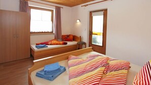 Ein Schlafzimmer mit Holzboden, einem Bett mit gestreifter Bettwäsche, einem Fenster mit Vorhängen und einem Kleiderschrank.
