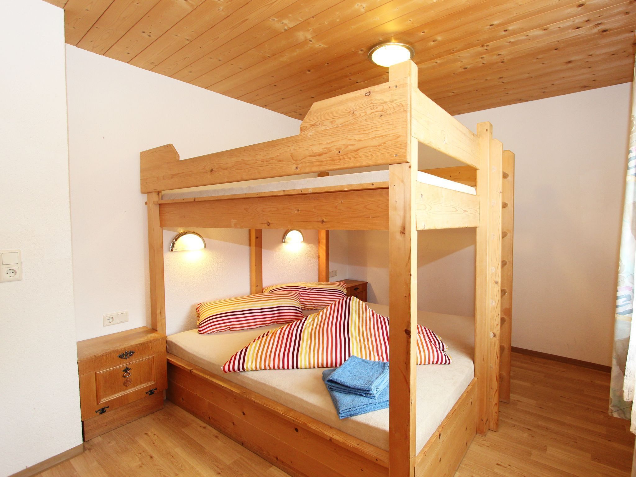 A bunk bed with wooden headboard and footboard, two bedside lamps, and a small wooden nightstand with drawers.