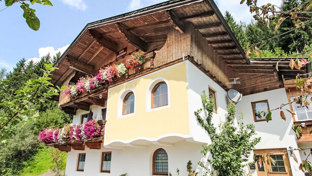 Ein zweistöckiges Gebäude mit Balkon, der mit Blumen geschmückt ist, einer Satellitenschüssel und einer Tür mit einem Schild.