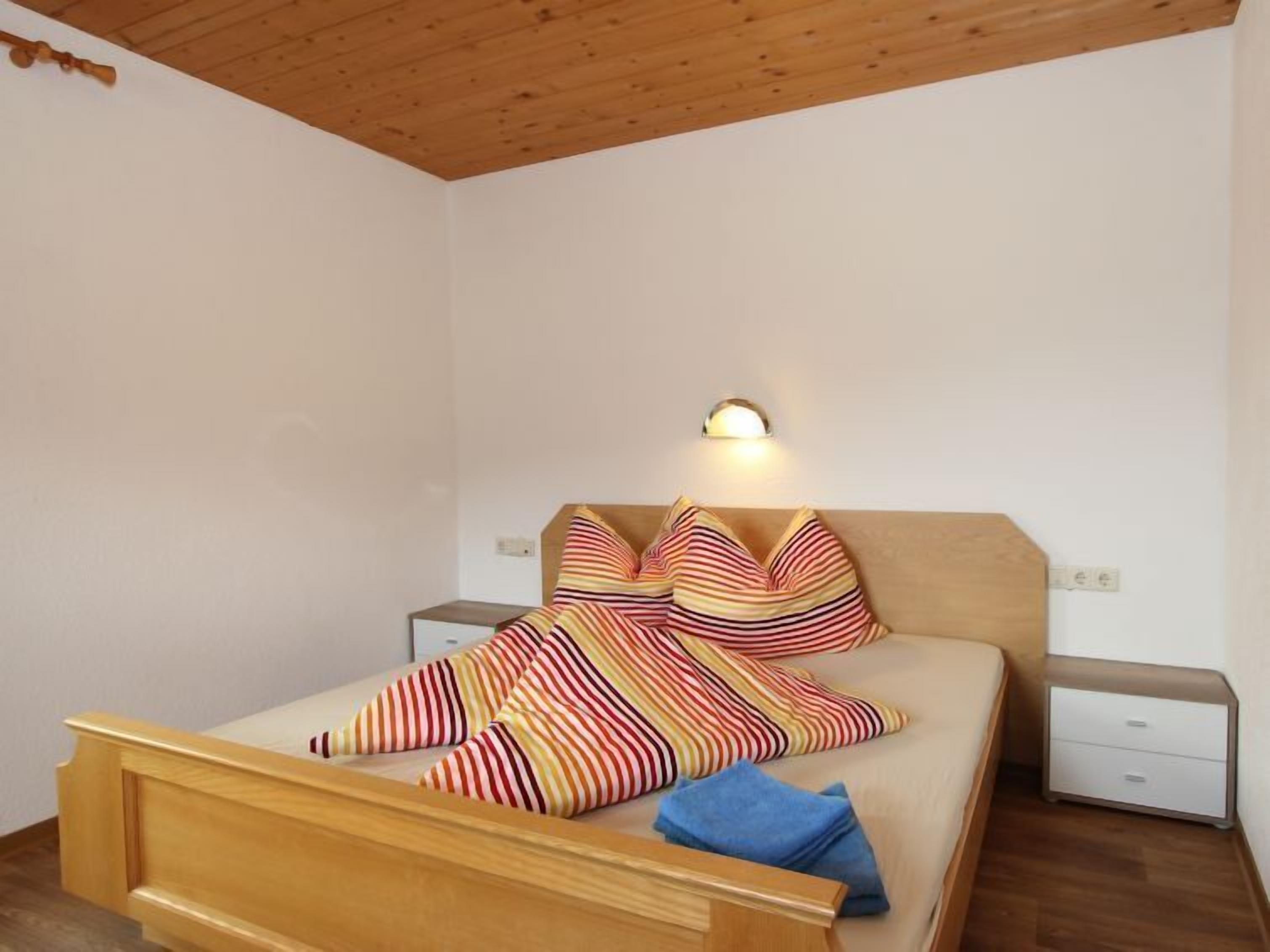 A bedroom with a wooden bed, striped bedding, a nightstand, and a wall-mounted light.