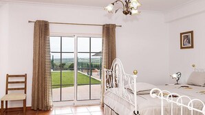 A bedroom with a bed, a chair, a window with curtains, and a view of the outdoors.