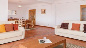 A spacious living room with two white sofas, a coffee table, and a dining area with a wooden table and chairs.