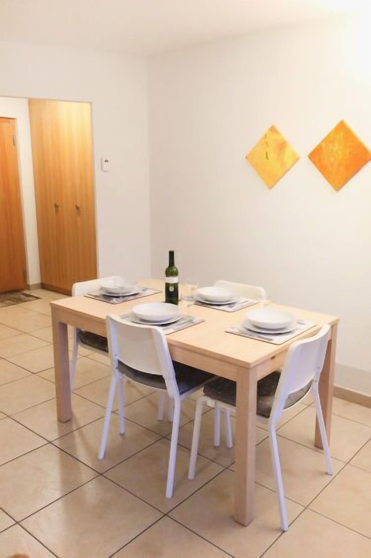 Ein Essbereich mit einem Holztisch, gedeckt für vier Personen, weißen Stühlen und einer Weinflasche auf dem Tisch.