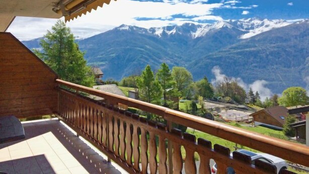 A balcony with a wooden railing overlooking a mountainous landscape with snow-capped peaks and a clear blue sky. - Viognier 5 by Interhome (Ovronnaz)