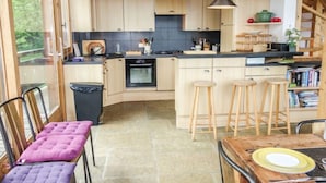 Una cocina moderna con armarios de madera, una isla central con taburetes, una mesa de comedor con sillas y vistas a zonas verdes.