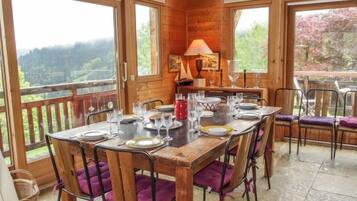 Une table à manger en bois, pouvant accueillir six personnes, entourée de chaises rembourrées de couleur violette, avec un banc en bois, et offrant une vue sur un paysage boisé grâce à de grandes fenêtres.