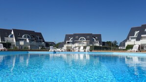 Une piscine avec des chaises longues et, en arrière-plan, un bâtiment au style architectural moderne.
