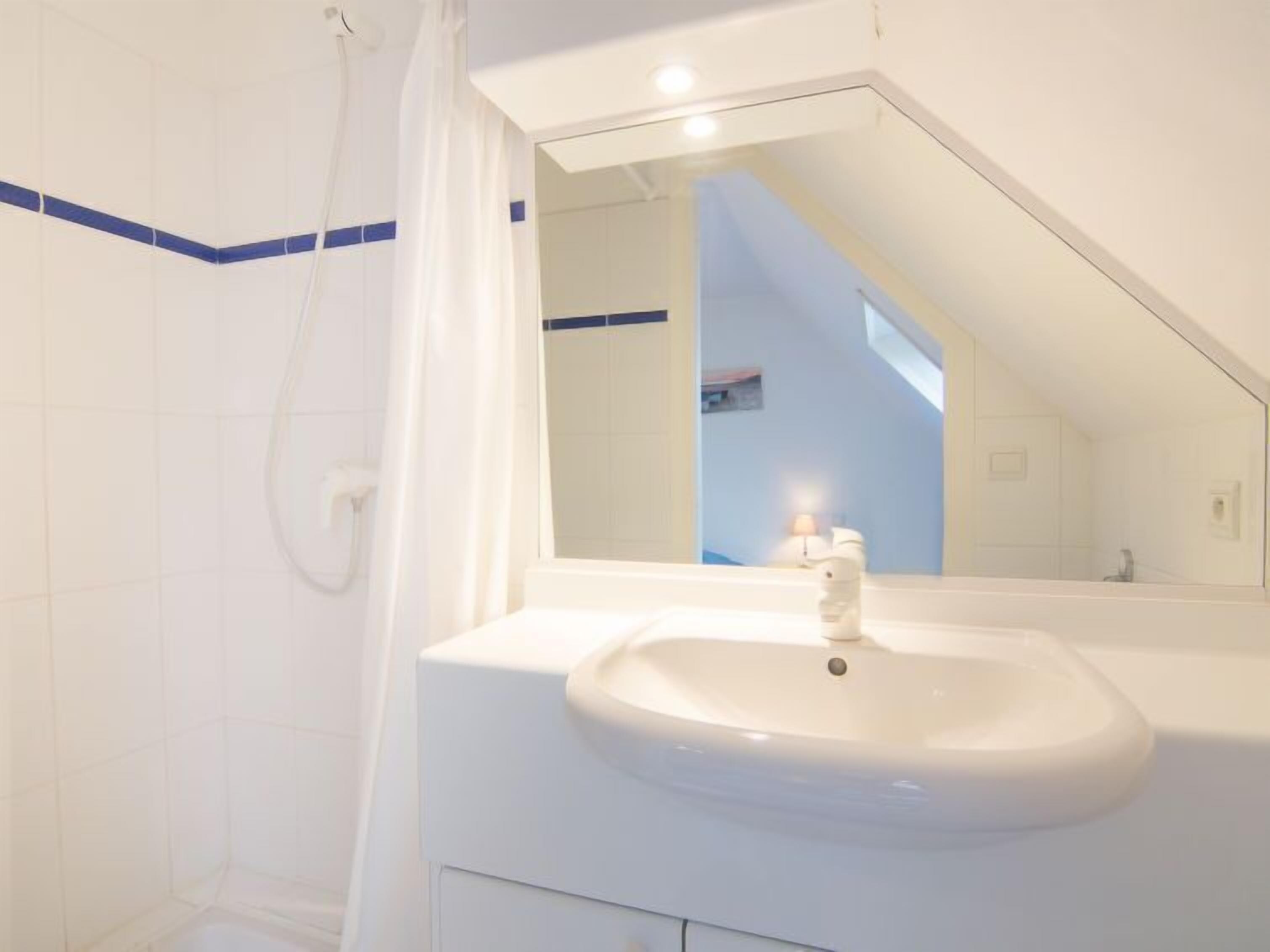 Un baño moderno con un lavamanos blanco, ducha y espejo que refleja una escalera.
