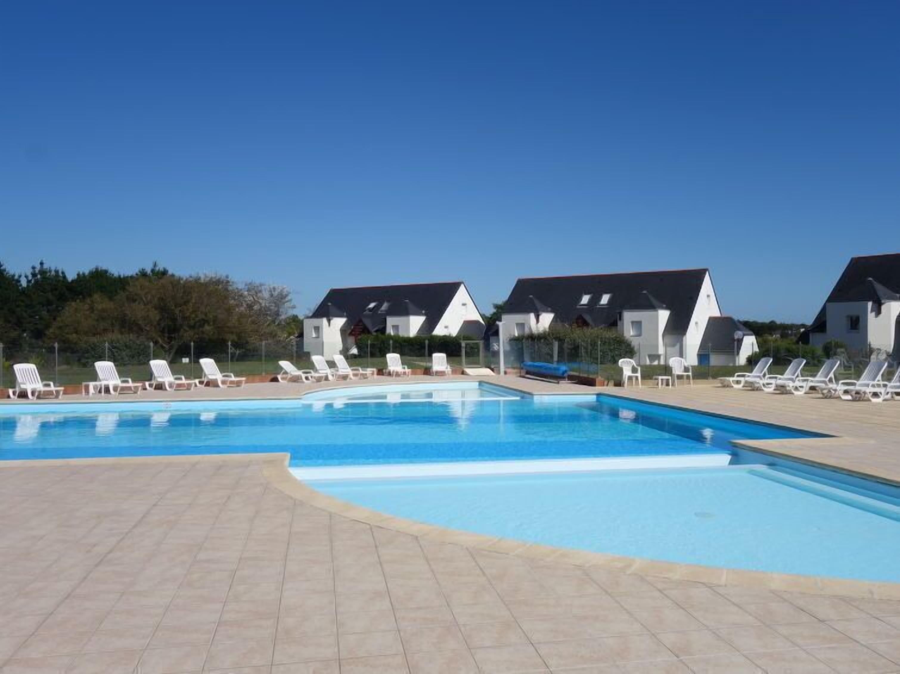 Piscina com espreguiçadeiras e edifícios brancos ao fundo.