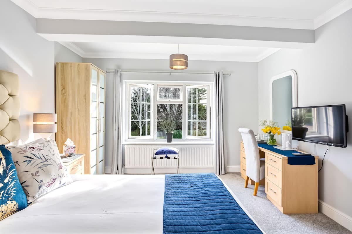 Un dormitorio con cama, escritorio, armario, televisor y ventana con cortinas.