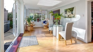 A spacious living area with a glass dining table, comfortable seating, and a view of the outdoors. - The Coast House B&B (Bognor Regis)