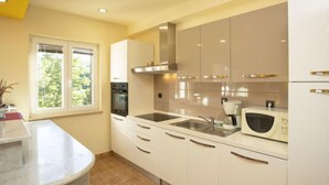A modern kitchen with white cabinets, a built-in oven, a microwave, and a window with a view of greenery.