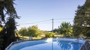 A circular swimming pool with a stone border, surrounded by trees and a clear sky.