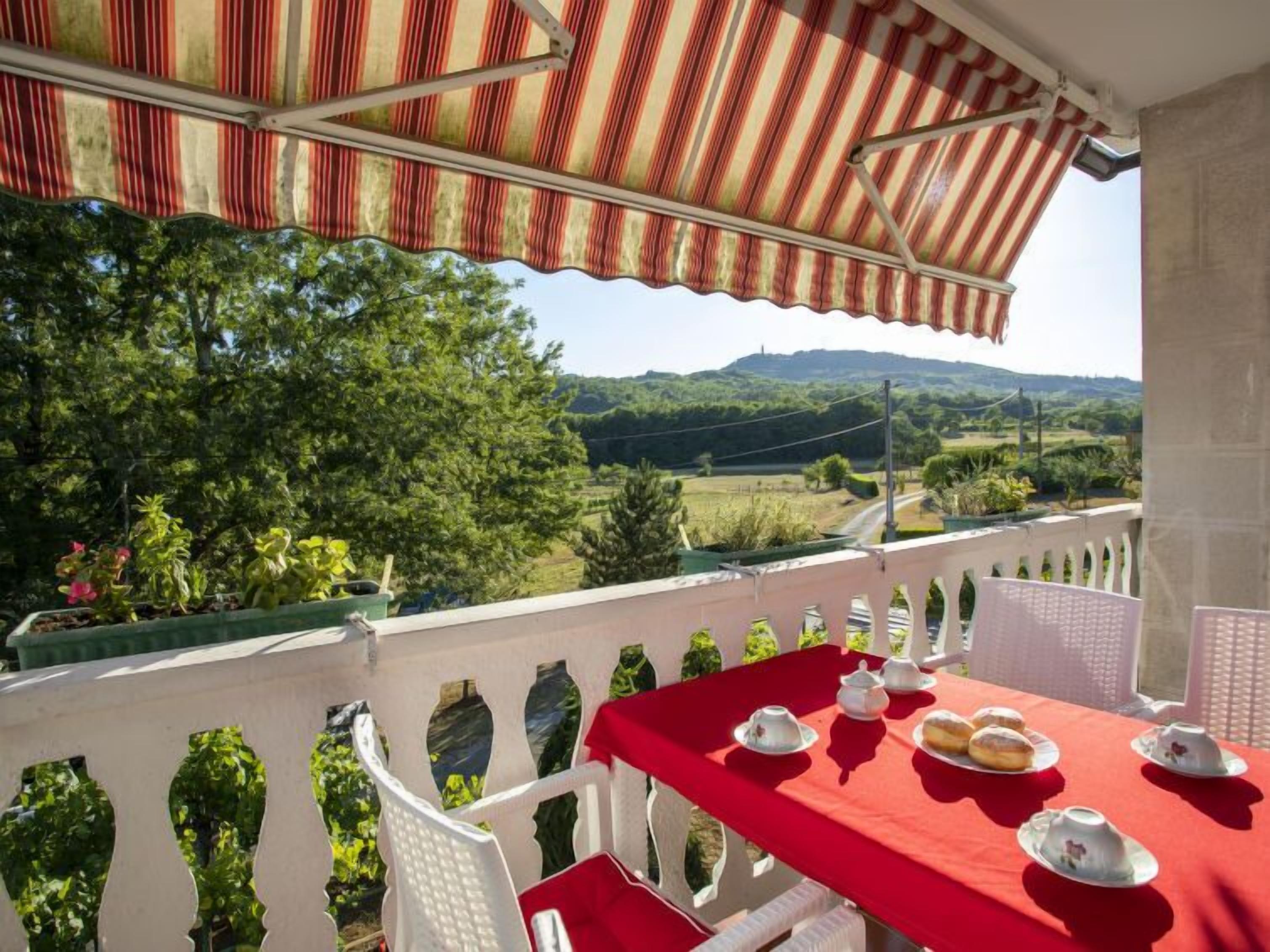Un balcon avec une table rouge dressée pour le thé, offrant une vue sur un paysage pittoresque.