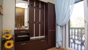A room with a large wardrobe, a mirror, a small table with a basket, and a vase with sunflowers.