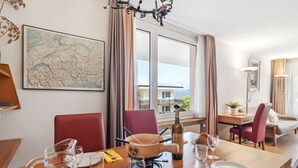 A dining area with a wooden table set for two, a map on the wall, and a view of the outside through large windows.