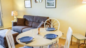 A dining area with a round table, white chairs, and blue plates. There is a brown sofa and a lamp in the background. - Terrasses d'Emeraude by Interhome (Dinard)