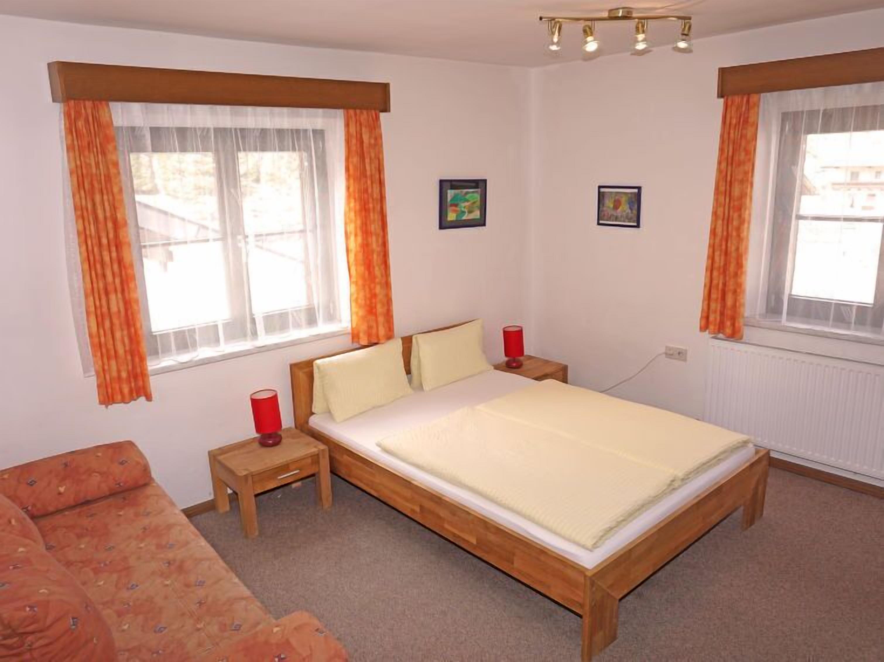 Un dormitorio con una cama de madera, dos mesitas de noche y dos ventanas con cortinas.