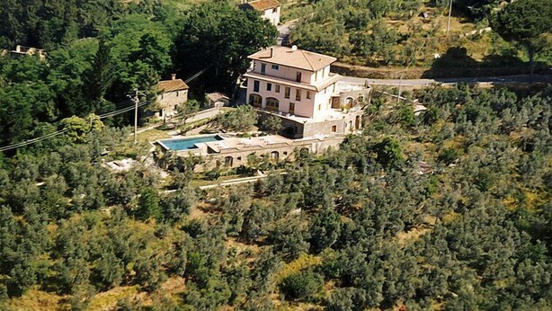 Un grand immeuble à étages, doté d’une piscine, entouré d’une forêt dense et situé dans un paysage vallonné.