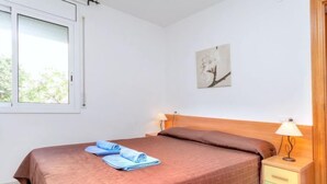 A bedroom with a bed, two bedside tables, a window, and a wall-mounted picture. - Palmiers I by Interhome (Llançà)
