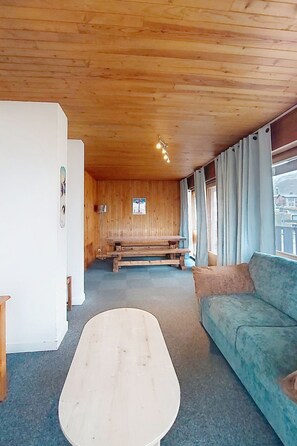 A room with a wooden ceiling, a blue sofa, a wooden bench, and a white table. - La Grande Casse (Lavachet) by Interhome (Tignes)