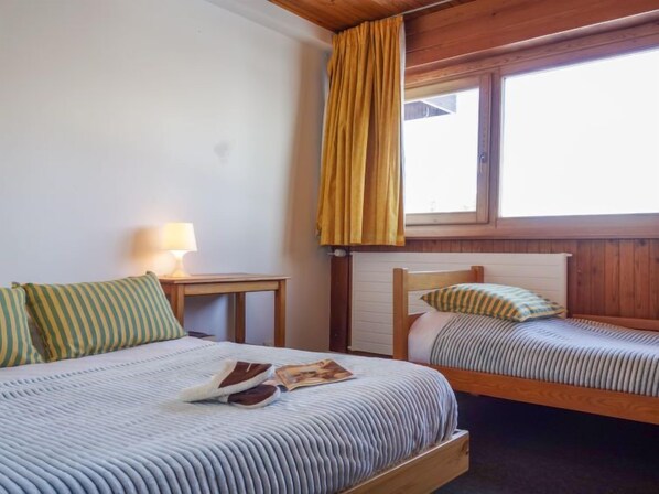 Une chambre avec deux lits, une table de chevet avec une lampe et une fenêtre avec des rideaux.