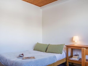 A small, neatly arranged bedroom with a single bed, a bedside table with a lamp, and a chair.