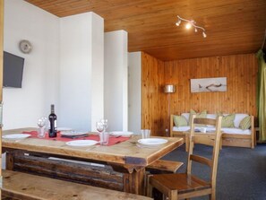 A wooden dining table set with plates, glasses, and a bottle, a sofa with pillows, and a wall-mounted picture.