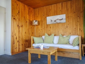 A wooden-paneled room with a white sofa, striped pillows, a small wooden table, and a lamp.