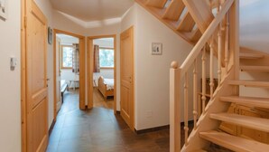 Una escalera de madera conduce a un segundo piso, un pasillo con puertas de madera y una cama al fondo.