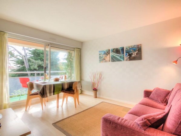 A modern living room with a pink sofa, a dining table with chairs, and a large window offering a view of the outdoors.