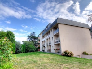 A multi-story building with a flat roof, balconies, and a well-maintained lawn.