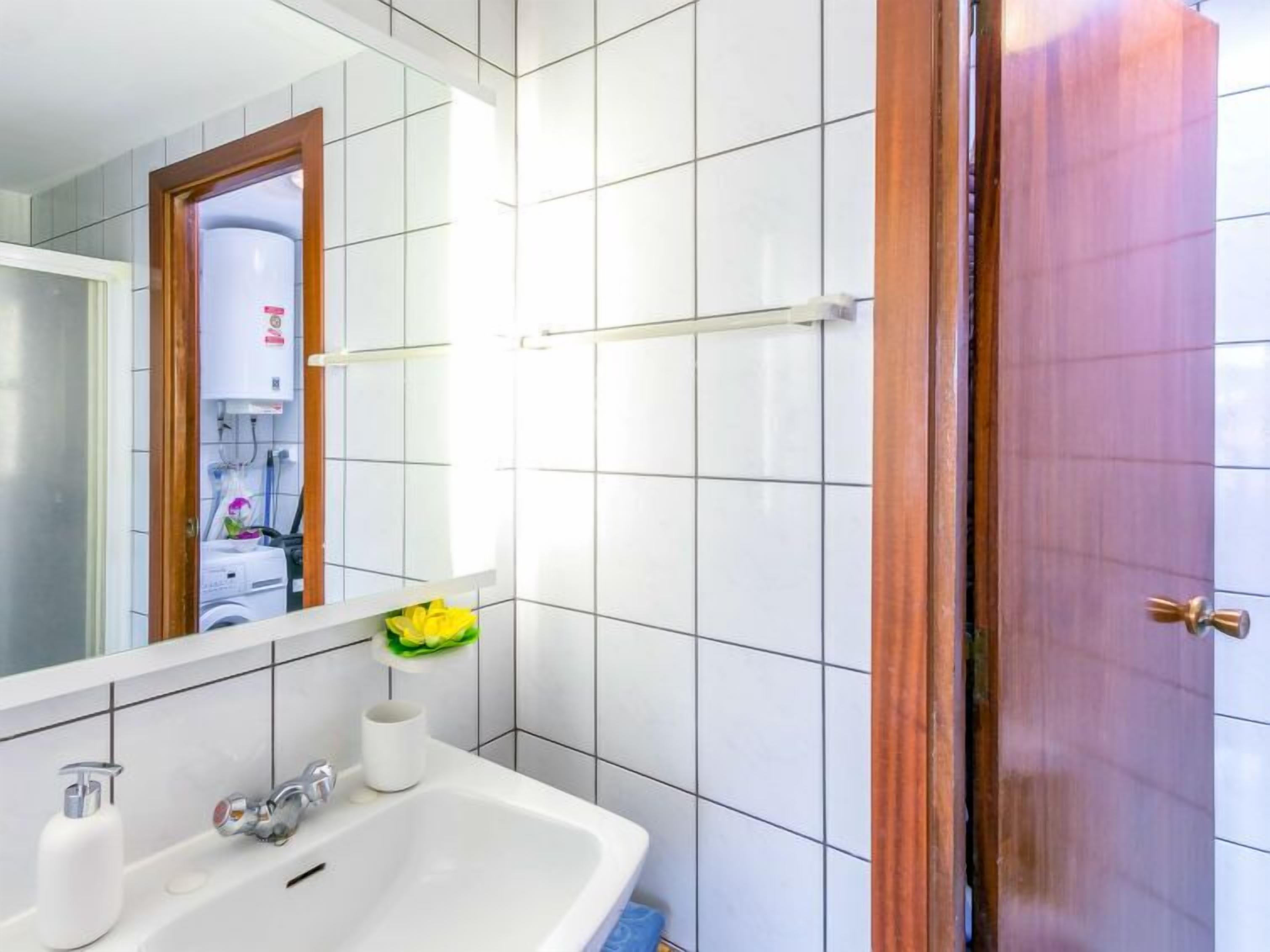 A bathroom with a white sink, mirror, and tiled walls.