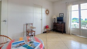 Ett rymligt rum med ett matbord, stolar, en tv och ett stort fönster med utsikt över grönområden.