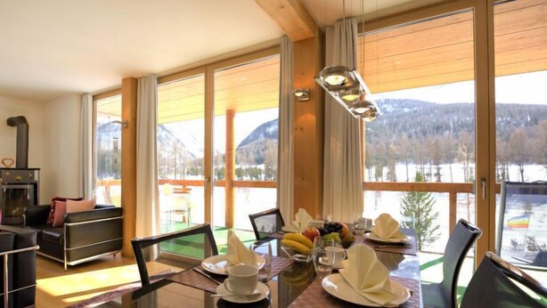 A dining area with a table set for two, a fireplace, and a view of a snowy landscape. - Chesa Lej by Interhome (Pontresina)