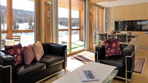 A modern living room with a black leather sofa, a coffee table, and a view of a snowy landscape through large windows. - Chesa Lej by Interhome (Pontresina)