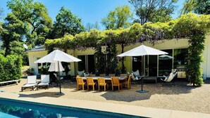 Un espace aménagé au bord de la piscine, avec une table et des chaises, des parasols et des chaises longues.