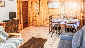 Una sala de estar acogedora con suelo de madera, un sofá, una mesa de centro, un televisor y un comedor con mesa y sillas.