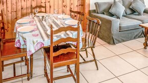 Un comedor con una mesa redonda preparada para cuatro personas, rodeada de sillas de madera. Se ve un sofá con cojines al fondo.