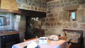 A rustic dining area with a stone wall, a wooden table set for two, and a vintage stove. - Le Pigeonnier by Interhome (Gramat)
