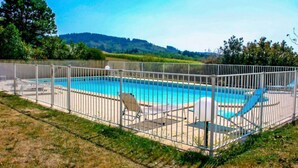 A rectangular swimming pool with a white fence, surrounded by grass and trees, with hills in the background. - Le Pigeonnier by Interhome (Gramat)