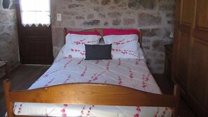 A bed with floral bedding, a wooden headboard, and a stone wall. - Le Pigeonnier by Interhome (Gramat)