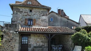 A stone building with a tiled roof, a small balcony, and a seating area with a table and chairs. - Le Pigeonnier by Interhome (Gramat)