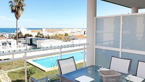 Un balcon avec une table en verre, des chaises et une vue sur une piscine et l’océan.
