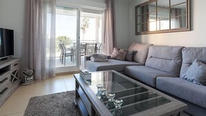 Un salon moderne avec un canapé gris, une table basse en verre et un téléviseur posé sur un meuble en bois.