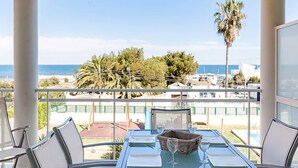 Un balcon avec une table dressée pour deux personnes, donnant sur une zone côtière bordée de palmiers et de bâtiments.