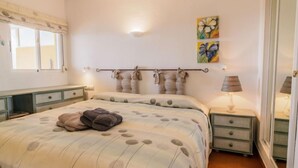Een slaapkamer met een bed, nachtkastjes, een lamp en kunst aan de muur.