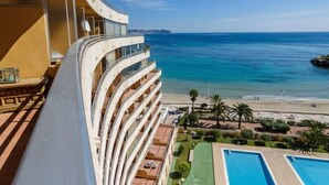 Een hoog hotel met balkons met uitzicht op een strand en een zwembad.